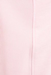 Detaily světle růžové látky, kde je vidět šev oddělující ribborově pletenou texturu vlevo a hladkou pletenou texturu vpravo.