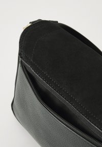 Borsa nera con fondo texture e parte superiore in morbido suede. Una chiusura con zip è visibile lungo il bordo, con eleganti accenti di cucitura in tutto il prodotto.