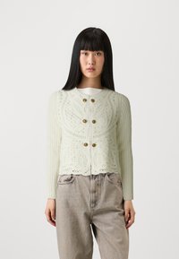 Cardigan lavorato a maglia verde chiaro con motivi intricati, dotato di due bottoni dorati e orlo a onde. Maniche lunghe e tessuto testurizzato.