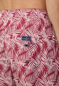 Costumi da bagno rossi con un motivo a foglie di palma bianche, vita elastica e tasca posteriore con etichetta blu navale con "HACKETT LONDON".