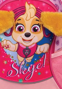 Roze rugzak met een cartoonhond met pluizige gele oren, een blauwe achtergrond met sterren en de naam "Skye" in glanzende letters.