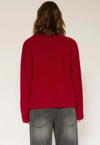 Pull en tricot rouge à coupe décontractée, avec des poignets et un ourlet côtelés, et un design de dos sans couture, associé à un jean large gris.