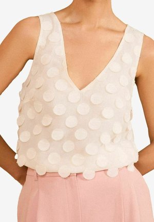 Bílý top bez rukávů s výstřihem do V a strukturovanými kruhovými vzory, spojený s vysokým pasem pastelově růžových kalhot.