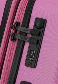 Maleta rígida rosa con una superficie texturizada, tiradores de cremallera negros dobles y un candado de combinación con una pantalla de tres dígitos.