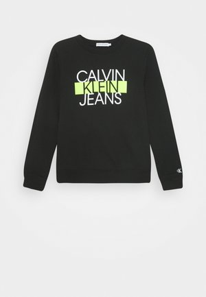 Schwarzes Sweatshirt mit langen Ärmeln und dem Schriftzug "Calvin Klein Jeans", wobei "Klein" in gelb-grün hervorgehoben ist, sowie einem kleinen "ck"-Logo am Bündchen.