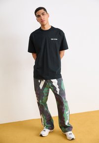 Svart bomulls t-skjorte med "Converse"-logo, sammen med flerfargede bukser med geometriske mønstre i lilla, grønn og hvit.