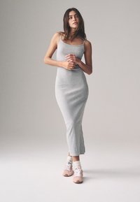 Sivá priliehavá midi šaty bez rukávov vyrobené z mäkkej elastickej látky, so strihom rovného strihu a bočnými rozparkami. Kombinované s ružovými teniskami.