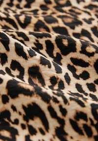 Tkanina s leopardím vzorem na světle hnědém pozadí s černými skvrnami, s hladkou texturou a jemným splýváním. Detailní pohled na vzor.