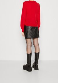 Rode trui met lange mouwen; zwarte leren minirok; visnetpanty's; zwarte platformlaarzen tot aan de knie. Glad materiaal, nauwsluitend ontwerp.