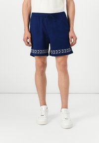 Navy blue shorts made of lightweight fabric, featuring a drawstring waist and a decorative white patterned trim at the hem.