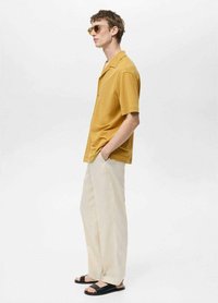 Short-sleeve mustard shirt with a relaxed fit, paired with light beige pants and black slide sandals, set against a plain white background.