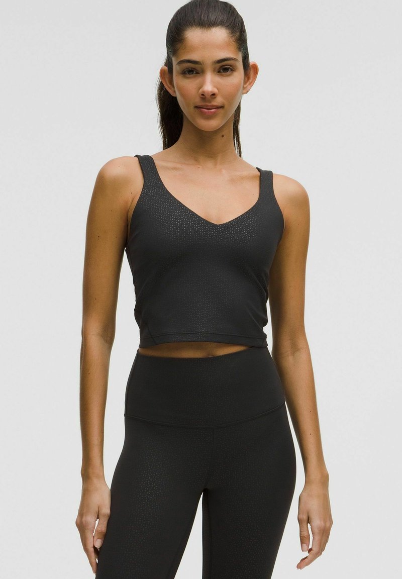 Sort atletisk crop top med V-hals og brede stropper. Fremstillet af glat, strækbart stof med subtile prikmønstre.