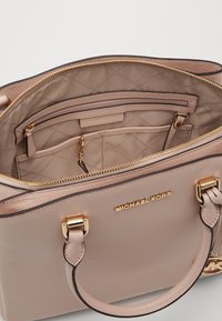 Lys lyserød lædertaske med guldfarvet hardware, lynlåslukning og quilted indvendig. Indeholder indvendige lommer og et navneskilt.