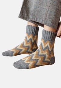 Mehrfarbige Stricksocken mit Zickzackmuster in Grau, Beige und Braun, mit einem gerippten Bündchen und weicher Textur.