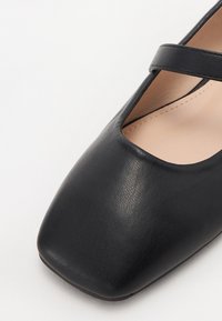 Chaussure Mary Jane en cuir noir avec un bout carré et une bride unique sur le cou-de-pied, semelle intérieure beige.