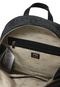 Schwarzer Stoff-Rucksack mit geprägtem Logo, goldener Reißverschluss und beigem Innenraum, der über eine Reißverschlusstasche und ein wiederholtes Muster des Markennamens verfügt.