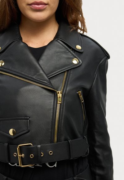 Giacca in pelle nera con hardware dorato, tasche con zip e vita con cintura. Caratterizzata da un colletto in stile motociclista e zip asimmetrica.