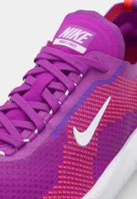 Fioletowe buty Nike charakteryzują się teksturowaną siateczkową cholewką z pomarańczowymi akcentami. Białe logo swoosh i płaskie fioletowe sznurówki dopełniają projekt.