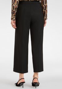 Czarne spodnie typu wide-leg z gładkiego materiału, z wysokim stanem i skróconym nogawkami. W połączeniu z czarnymi sandałami na obcasie.