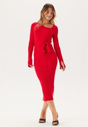 Rode geribde jurk met een aansluitende silhoeët, lange mouwen, een ceintuur in de taille en een lengte tot de knie. Gladde textuur en uitsparing bij de manchetten.