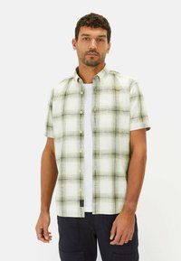 Korte mouw geblokt shirt met groen en wit patroon, voorzien van een knoopsluiting en lichte stof. Draagt over een wit T-shirt.