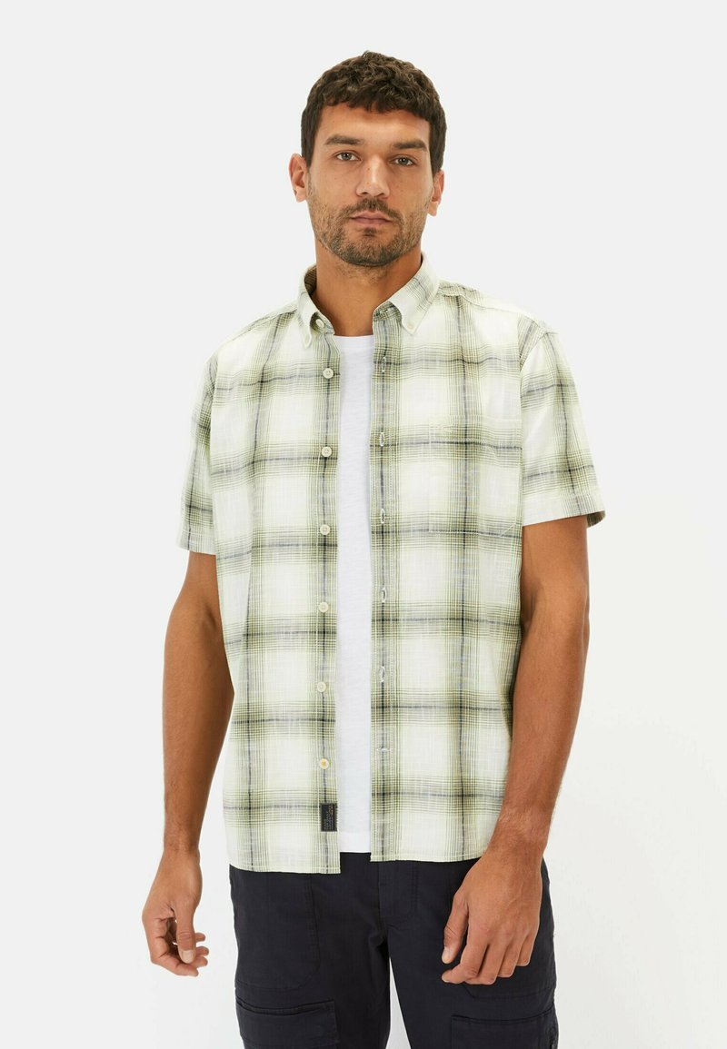 Korte mouw geblokt shirt met groen en wit patroon, voorzien van een knoopsluiting en lichte stof. Draagt over een wit T-shirt.
