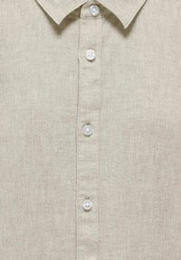 Camicia in lino beige chiaro con colletto, dotata di chiusura frontale con bottoni bianchi, che evidenzia un tessuto testurizzato.