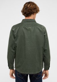 Grünes Cordhemd mit Kragen, langen Ärmeln und einem geknöpften Manschetten, versehen mit vertikalen Streifen und einem abgerundeten Saum. Rückansicht gezeigt.