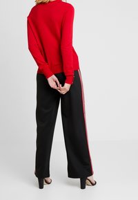 Röd långärmad tröja med ribbade muddar, matchad med svarta vida byxor med röda sidostråk och subtila dragkedjor vid nederdelen.