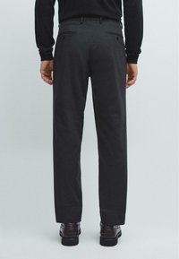 Černé kalhoty s rovně střiženým střihem, které mají dvě zadní kapsy s knoflíkovým zapínáním a hladkou texturu látky. Boty jsou viditelné níže.