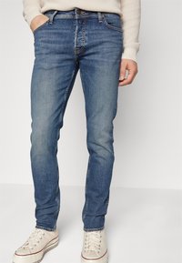 Blå denimjeans med en något blekt finish, rak bendesign och klassisk femficksstil. Matchas med beige sneakers.