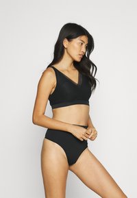 Black bra and high-waisted brief set made from smooth fabric. Bra features a V-neck with lace accents. Briefs have a classic silhouette.