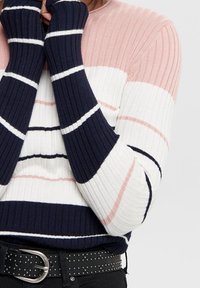 Pull en tricot côtelé présentant des rayures horizontales roses, blanches et bleu marine, avec des poignets allongés et un col rond, associé à une ceinture à clous.
