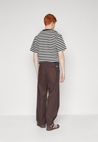 T-shirt à manches courtes à rayures noires et blanches, associé à un pantalon ample marron avec des poches arrière et une étiquette de marque visible.