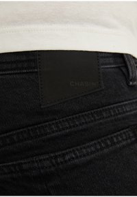 Mustat farkut, joissa on teksturoitu pinta, varustettuna takaselässä näkyvällä "CHASIN'"-nahkalaminoidulla merkinnällä ja näkyvillä ompelusaumoilla.