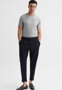 Tricou gri cu mânecă scurtă, pantaloni în culori bleumarin pliați cu mansete răsucite, mocasini maro. Design simplu, textură moale, croială lejeră.