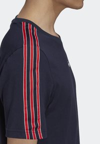 Mörkblå t-shirt med korta ärmar och röda och vita vertikala randiga detaljer på axlarna. Rundhalad design, tillverkad av bomullstyg.