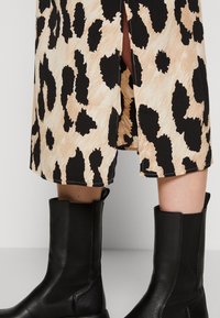Falda de estampado de leopardo en tonos marrón y negro con una abertura lateral, combinada con botas de cuero negro hasta la rodilla, que presentan materiales texturizados y un diseño elegante.