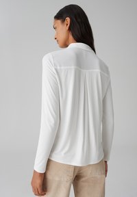Witte blouse met lange mouwen en een kraag, met een plooidetail aan de achterkant en van glad, lichtgewicht materiaal. Gecombineerd met beige corduroy broek.