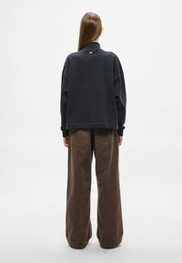 Σκούρο γκρι φαρδιά φούτερ με ψηλό γιακά και μικρό λογότυπο στο πίσω μέρος, συνδυασμένο με χαλαρά καφέ παντελόνια από κορντόρι με πίσω τσέπες.