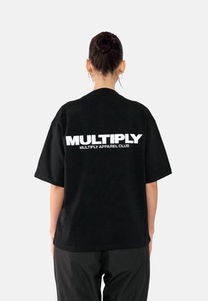 Black oversized t-shirt featuring bold white text "MULTIPLY" and "MULTIPLY APPAREL CLUB" on the back. Short sleeves, relaxed fit, cotton material.