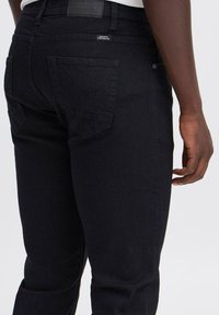 Donkerdenim jeans met een getailleerd ontwerp, voorzien van achterzakken met ruitvormige stiksels en een gladde textuur, gecombineerd met een zwarte tailleband.