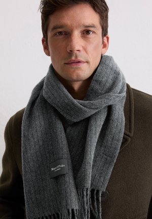 Gray ribbed scarf made of soft wool, featuring fringed edges and a black label with "Marc O'Polo" logo, wrapped around the neck.