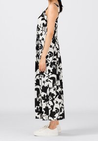 Czarna i biała długa sukienka maxi w kwiaty, wykonana z lekkiego materiału, z cienkimi ramiączkami i luźnym krojem, zestawiona z białymi trampkami.