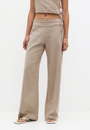 Vrouw draagt beige geribbelde wijde broek en bijpassende korte tanktop, staat op blote voeten met sandalen met vierkante neus.