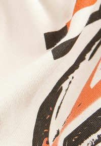 Baumwollstoff mit weißem Grund, der abstrakte Muster in Orange und Schwarz aufweist. Die Textur ist glatt mit einem leicht gerippten Aussehen.