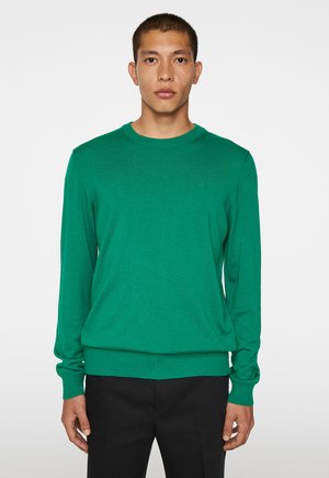 Grønt strikket sweater med lange ærmer, ribbede manchetter og kant. Har en rund halsudskæring og et diskret logo på brystet.