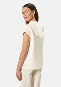 Haut à capuche blanc avec des manches courtes et une coupe décontractée, présentant une texture lisse et des détails de couture subtils à l'arrière.