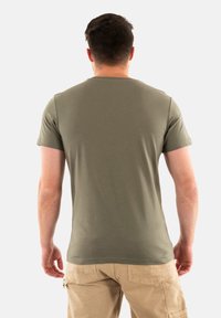 Camiseta de manga corta verde oliva hecha de tela suave, con un cuello redondo clásico y un ajuste relajado. Combinada con pantalones cargo beige.
