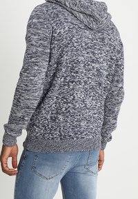 Mörkblå stickad hoodie med en strukturerad, melerad mönstring. Har en avslappnad passform, långa ärmar och ribbade muddar och fåll.